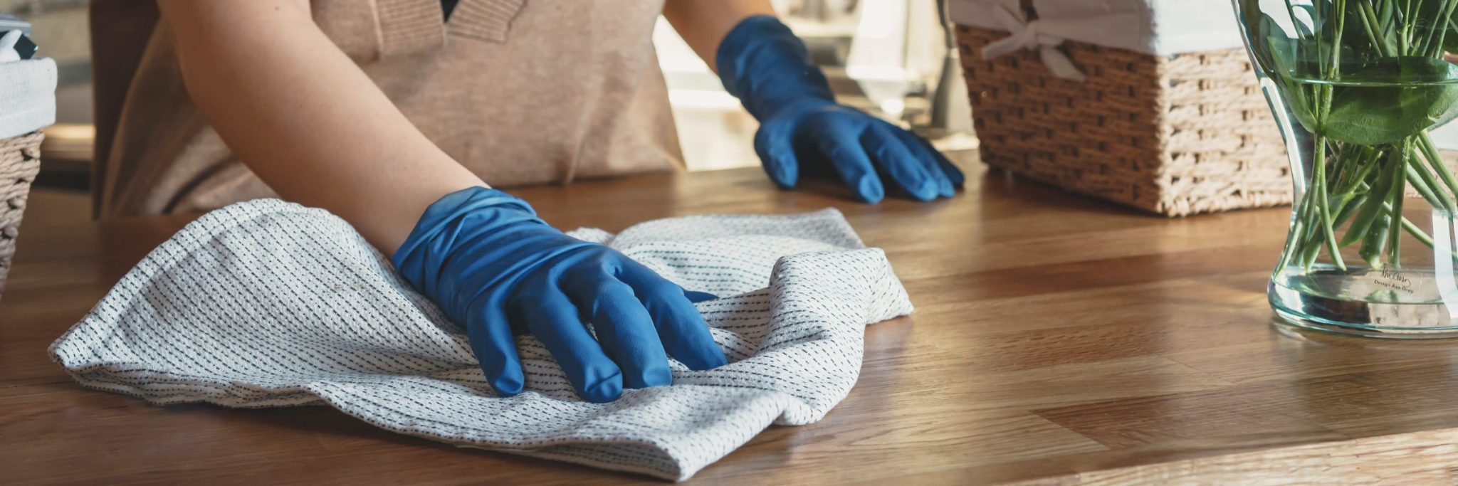 Person in blue gloves cleaning wooden table surface with gray cloth